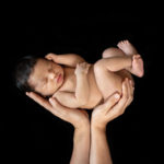 Nouveau-né en position foetale dans les mains de sa maman sur fond noir
