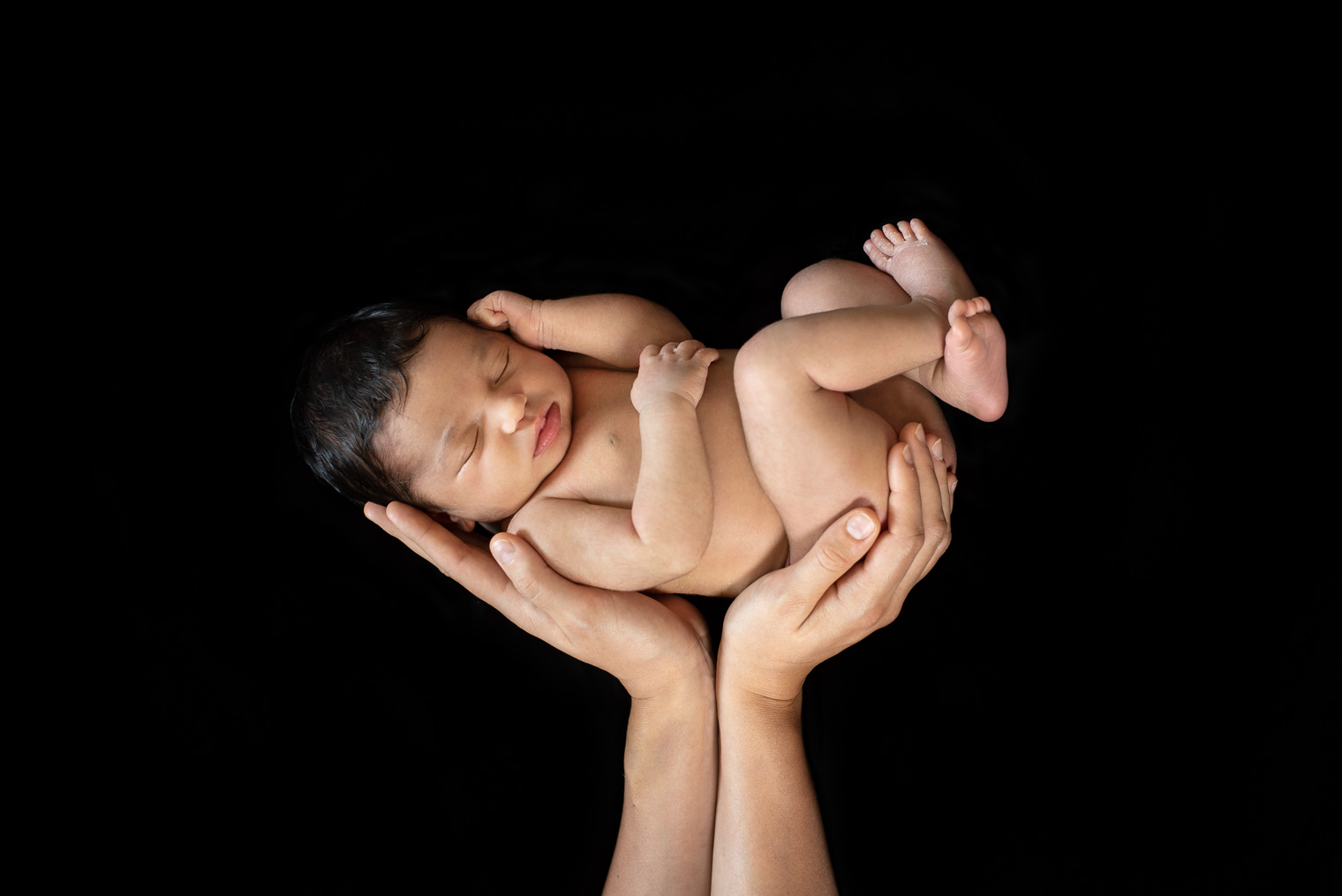 Nouveau-né en position foetale dans les mains de sa maman sur fond noir