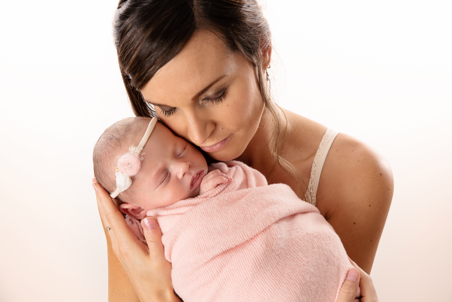 Nouveau-né fille endormie et emmaillotée dans un tissu rose, elle est dans les bras de sa maman
