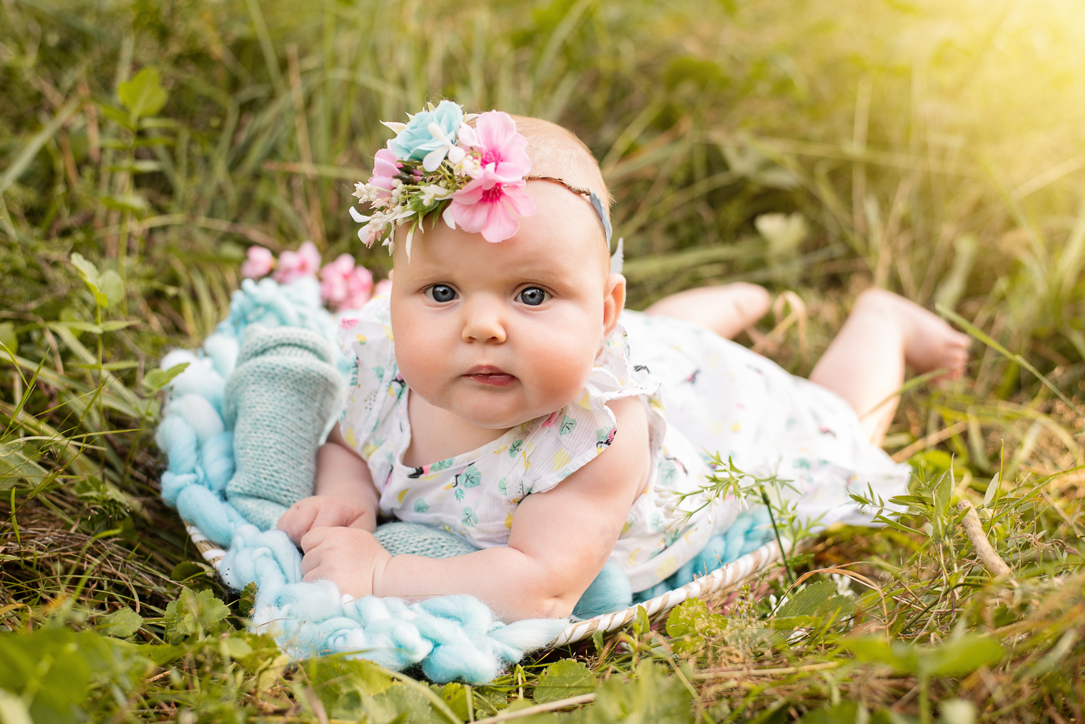 Bébé fille avec une robe à fleurs et un bandeau assorti, allongé sur le ventre sur une couverture en laine bleue posée dans l'herbe