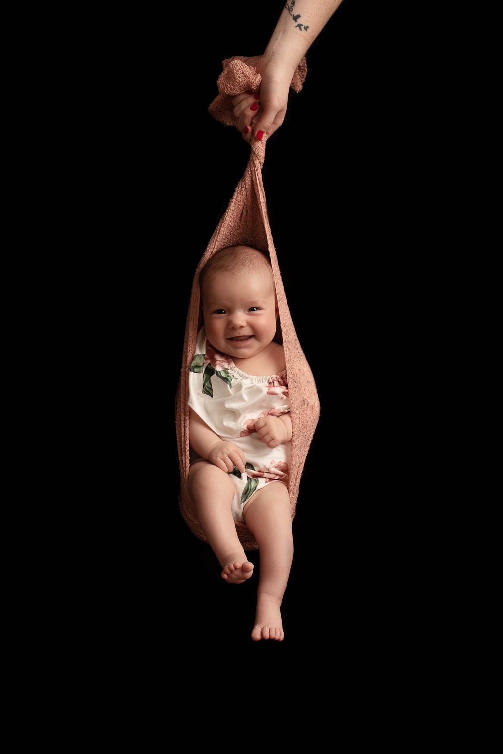 Bébé fille qui fait de la balançoire dans un tissu rose soutenue par la main de sa maman
