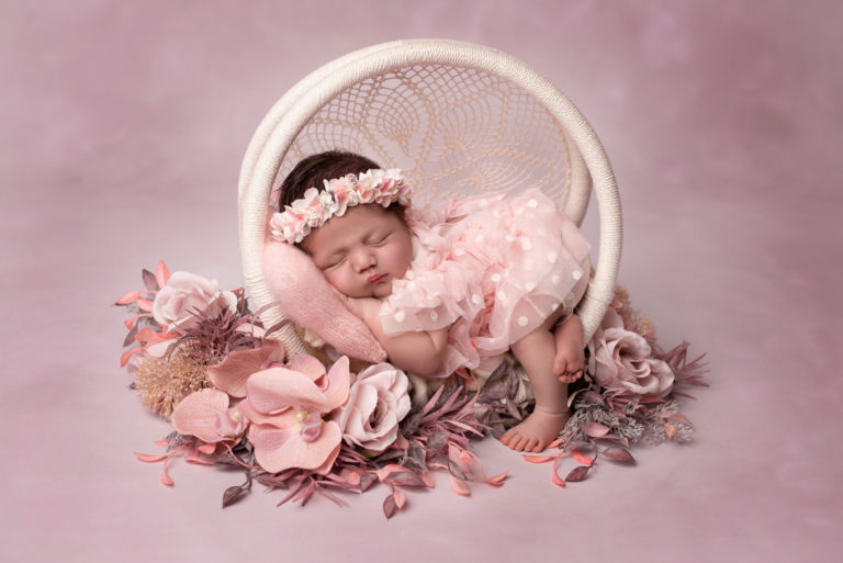 Nouveau-né fille paisiblement endormie avec une robe en tulle rose entourée de fleurs